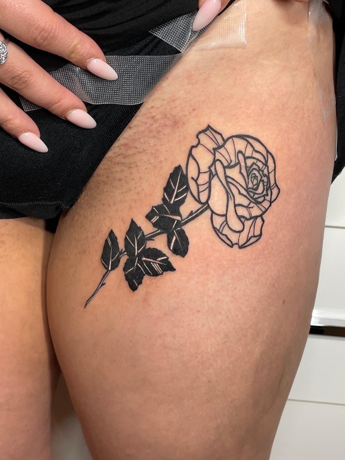 Blackwork tattoo bold rose with stem and leaves on upper arm in Los Angeles