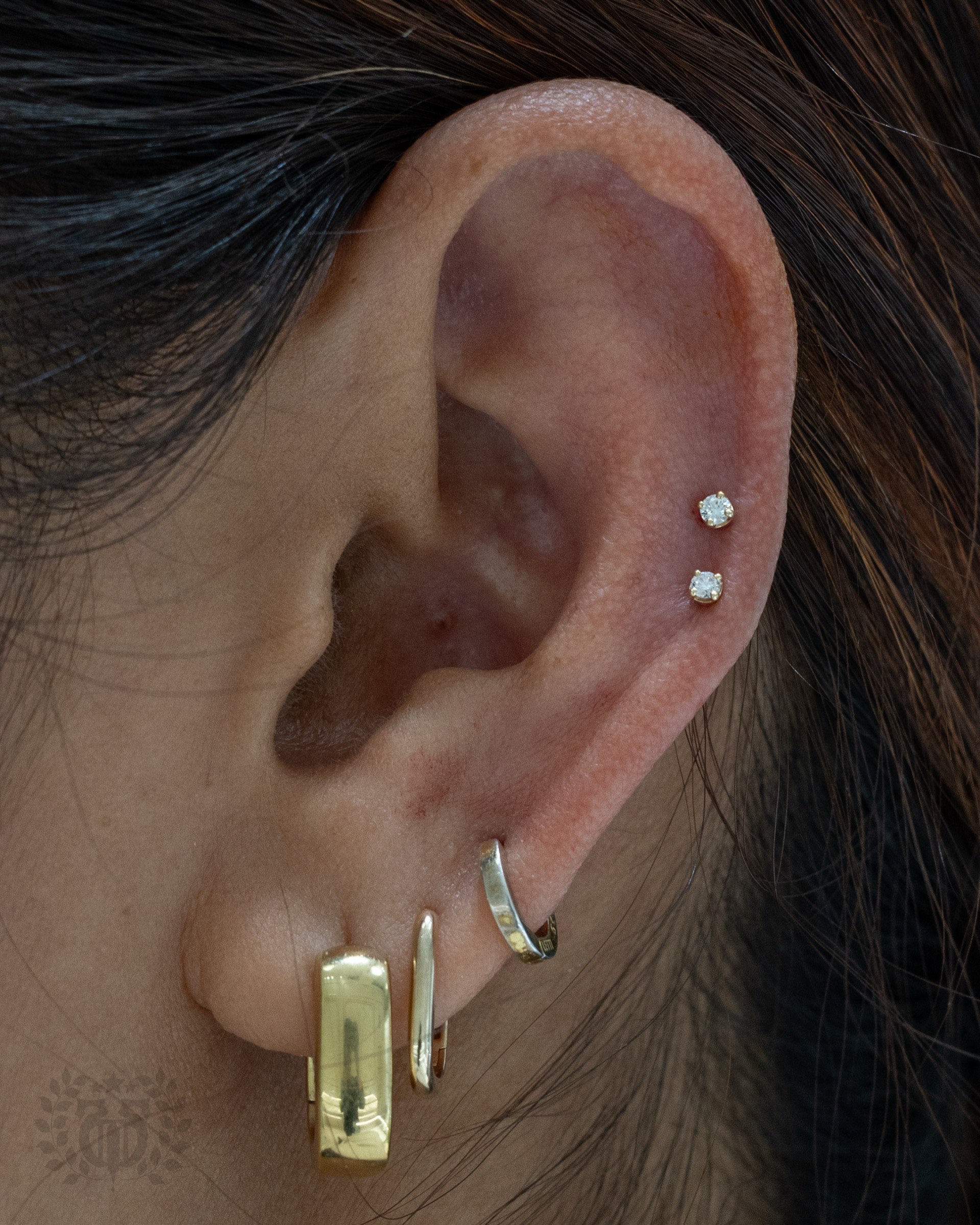 Mid-ear double CZ snakebite cartilage studs with gold lobe earrings at Apollo Studio Los Angeles