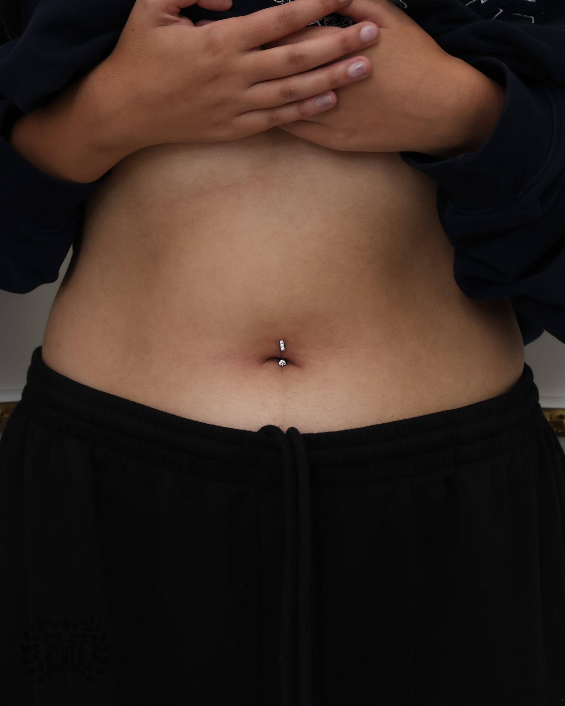 Belly button piercing with prong-set CZ curved barbell on client at Apollo Tattoo and Piercing
