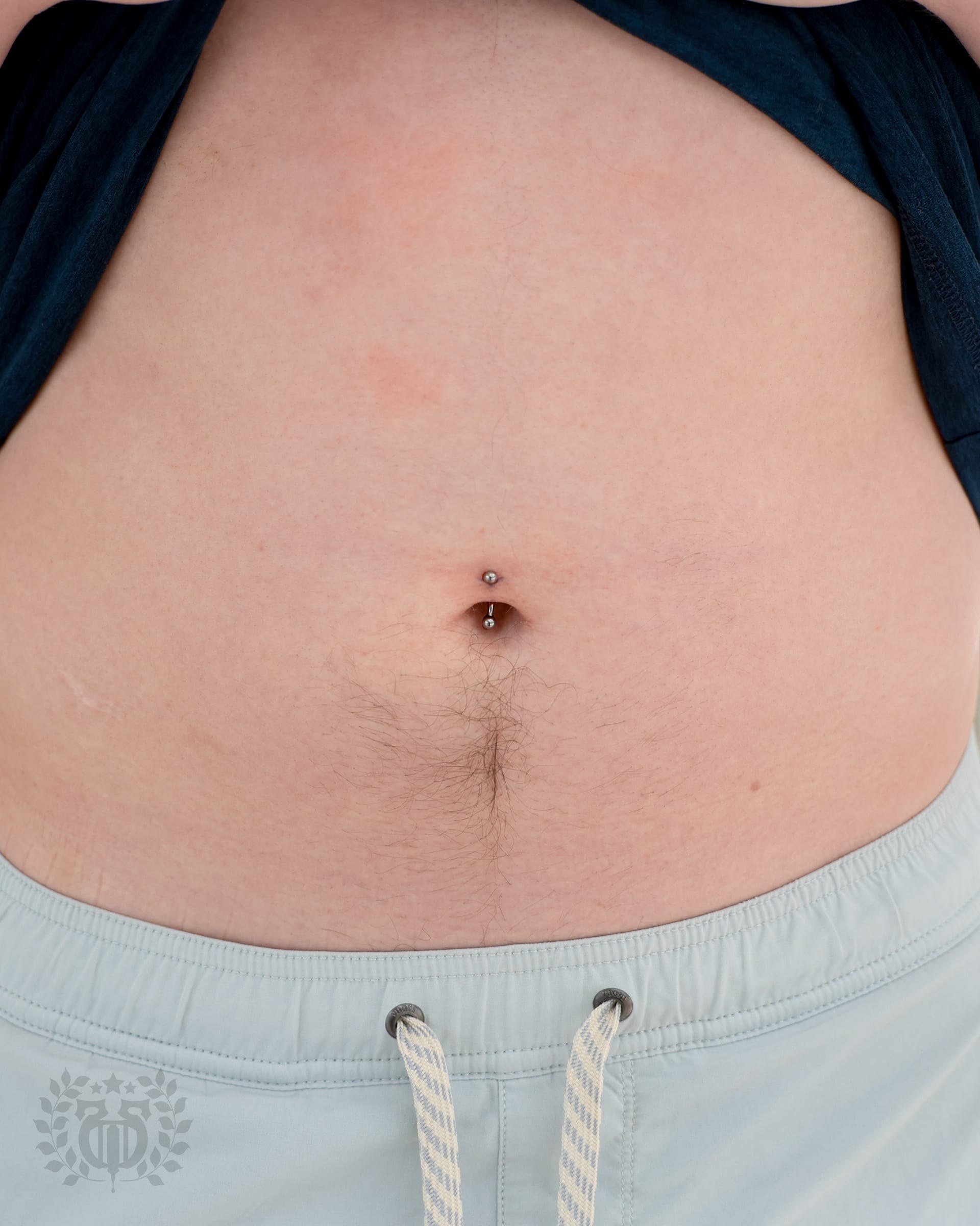 Close-up navel piercing with double prong-set CZ curved barbell at Apollo Studio