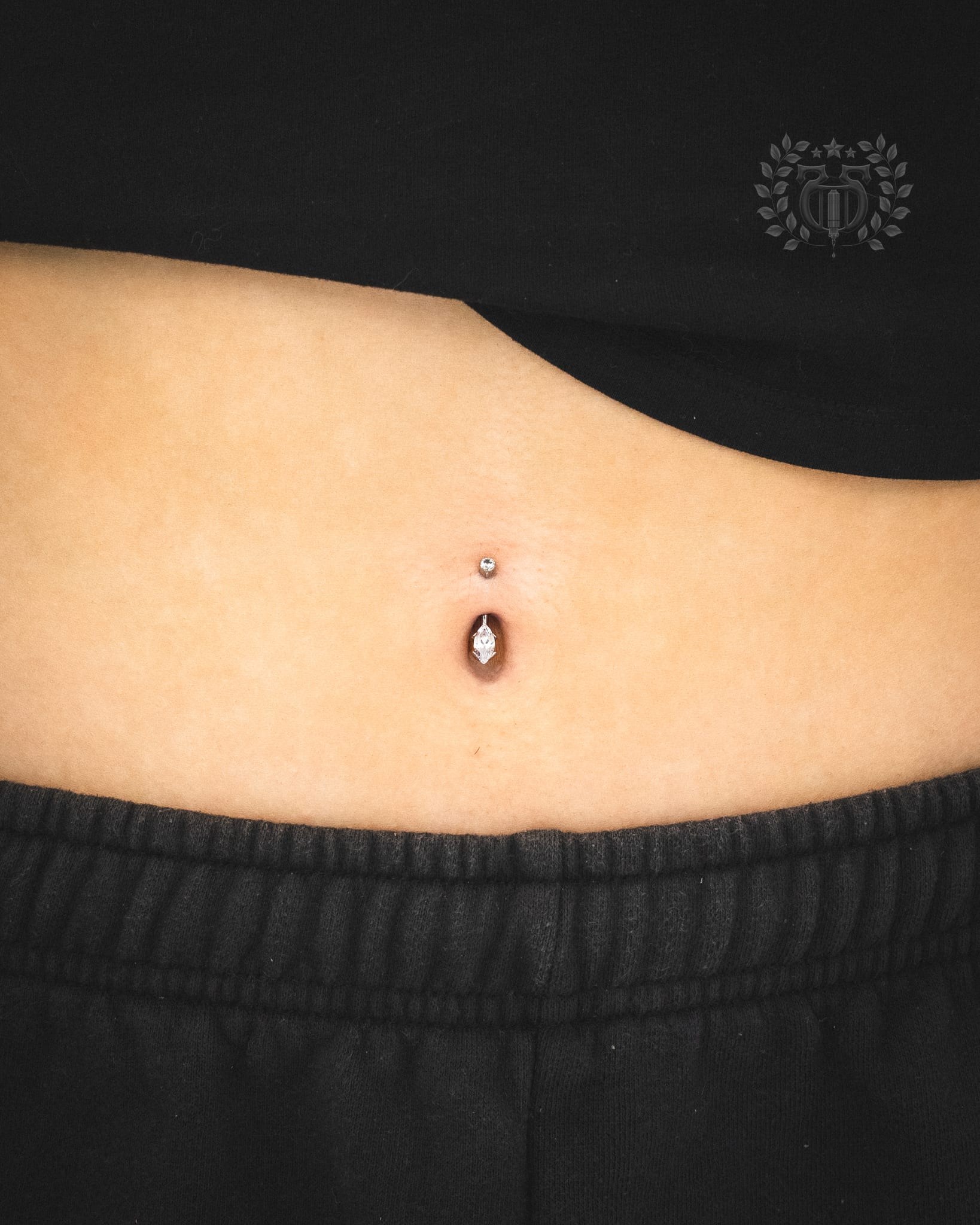 Navel piercing with gold diamond-shaped CZ end on curved barbell at Apollo Tattoo and Piercing