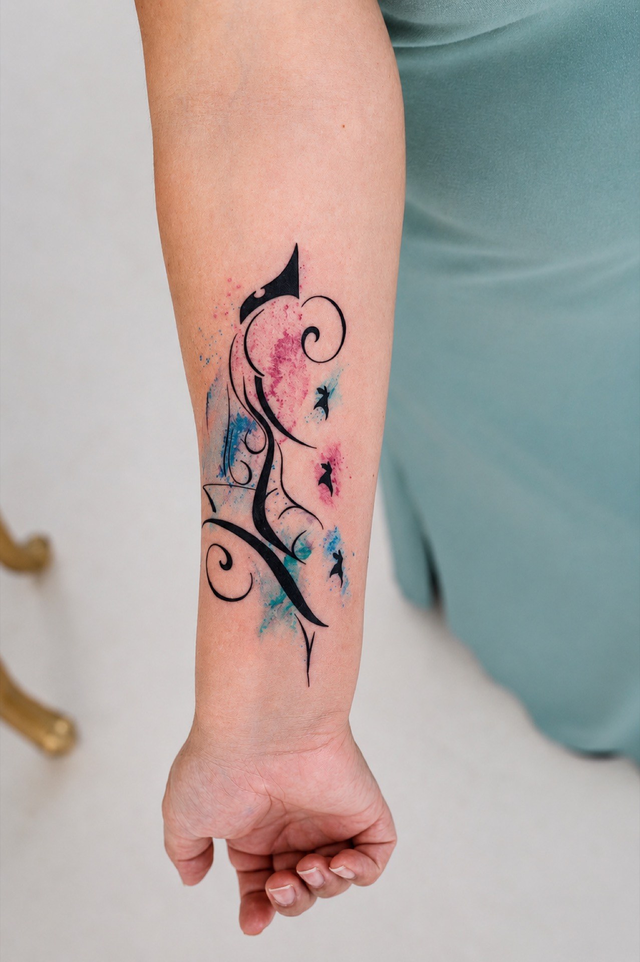 Abstract watercolor tattoo with black linework and pink and blue splashes on the forearm at Apollo Studio Los Angeles